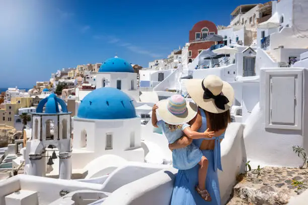 Photo of A tourist mother and her daughter looking at the whitewashed houses of the village Oia