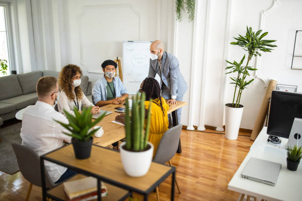 istock Manager and employees with protective face masks talking about business strategy during business meeting at office 1326281529