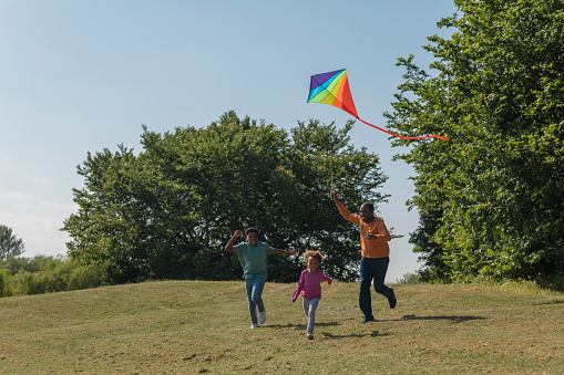 A grandad and his two grandchildren having a great time and running down a hill in the North East of England. They are pulling behind them a multicoloured kite and all smiling with glee as they enjoy quality time with Grandad.