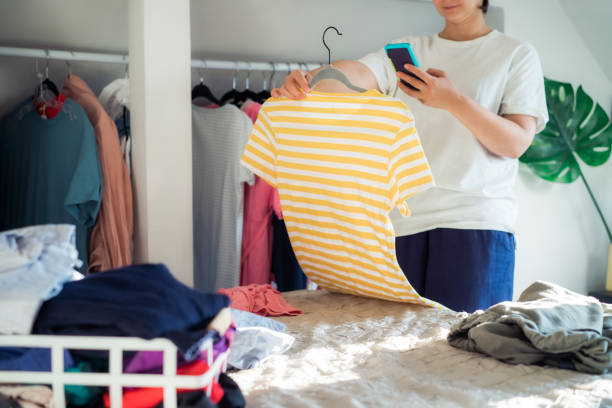 femme prenant une photo de t-shirt à l’aide de son smartphone pour vendre ou donner ses vêtements. désencombrer les vêtements, trier et nettoyer. réutilisation, concept d’occasion. consommateur conscient - garment photos et images de collection