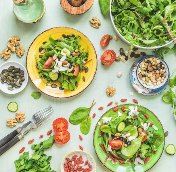 Plates with green salad on kitchen table background with forks and ingredients: nuts, seeds, young leaves, olives oils dressing. Top view. Dieting. Summer cuisine. Healthy home food