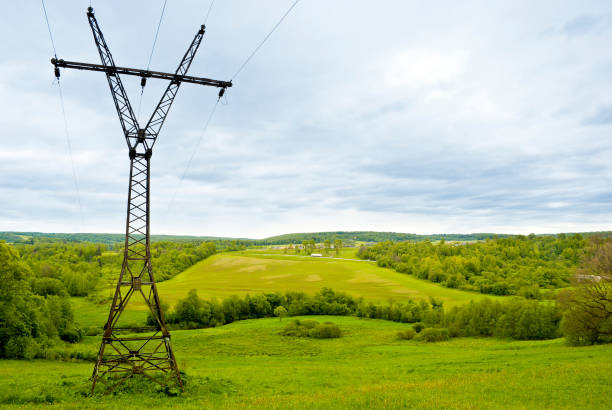 Rural landscape. Power line tower on hilly terrain. Forest fields and cloudy skies with clouds