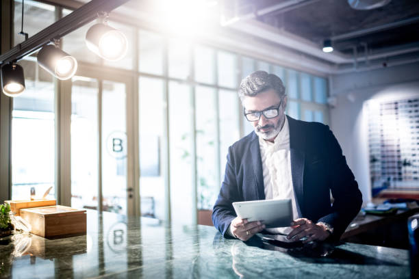 Mid adult man working using digital tablet Mid adult man working using digital tablet senior management stock pictures, royalty-free photos & images