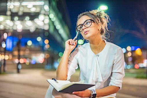 Young businesswoman thinking about something while holding a notebook during the night