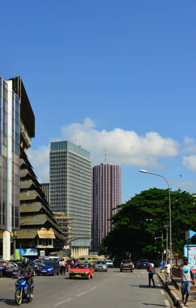 Ministry of Agriculture, the CAISTAB Building - cars and people on Boulevard Botreau Roussel, Abidjan, Ivory Coast Abidjan, Ivory Coast / Côte d'Ivoire: CAISTAB building, government tower on Boulevard Botreau Roussel, houses the Ministry of Agriculture and the Café-Cacao Council - completed in 1984, architects Bernard Nivet, Robert Boy - its name derives from the now defunct agricultural regulator, the Agricultural Production Price Stabilization and Support Fund (CSSPPA), better known by the diminutive Caistab, the Ivorian state body responsible for managing the cotton , cocoa and coffee sectors. To right is the Postel 2001 tower, another government building, both are managed by the government real-estate agency the SOGEPIE. abidjan skyline stock pictures, royalty-free photos & images