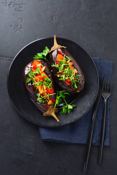 istock Baked stuffed eggplant with different vegetables, tomato, pepper, onion and parsley on a black stone or concrete table background. Top view 1326303933