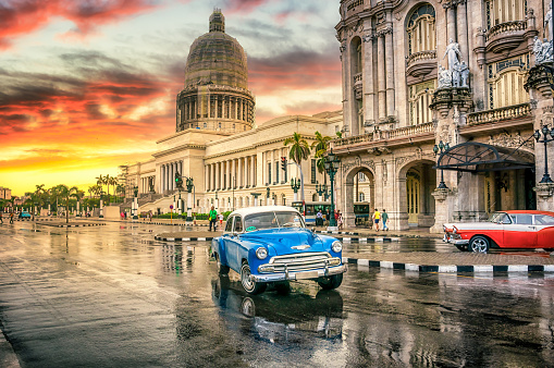 Blue and red Vintage Car Moving In Front Of El Capitolio at sunset in Havana, Cuba