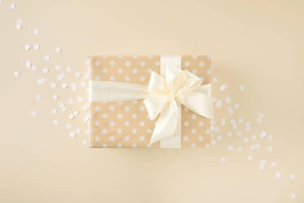beige gift wrapped in dotted paper with white bow on beige background