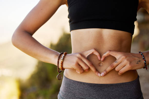 foto recortada de una mujer joven formando una forma de corazón sobre su estómago - sistema digestivo humano fotografías e imágenes de stock