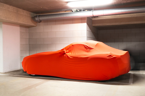 Expensive new car with orange cover for protection parked in garage,modern sports car