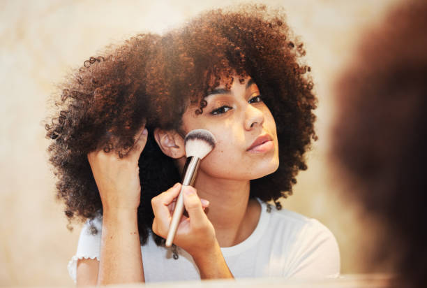 shot of a beautiful young woman using a makeup brush on her face - make up cosmetics women make up brush imagens e fotografias de stock