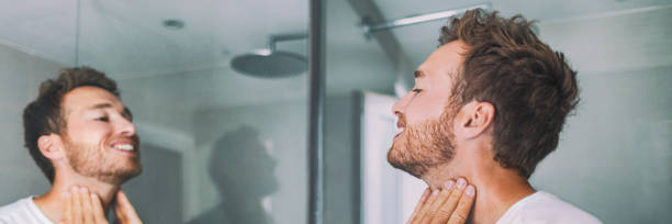 homme mettant après rasage lotion de parfum ou crème de soins de la peau pour les peaux sensibles après rasage barbe regardant dans le miroir de salle de bain sur le cou. beauté masculine, concept de soin de la barbe - human skin dry human face peeling photos et images de collection