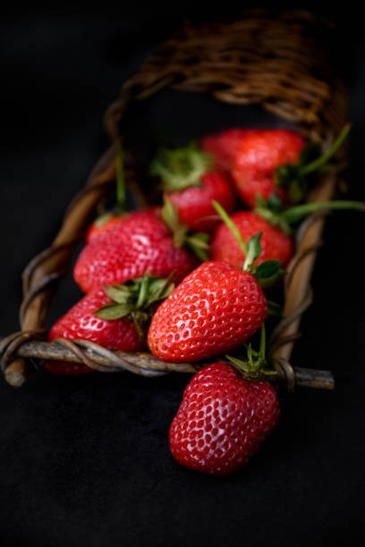 istock Ripe red strawberries scattered from wicker basket on dark background 1326321637