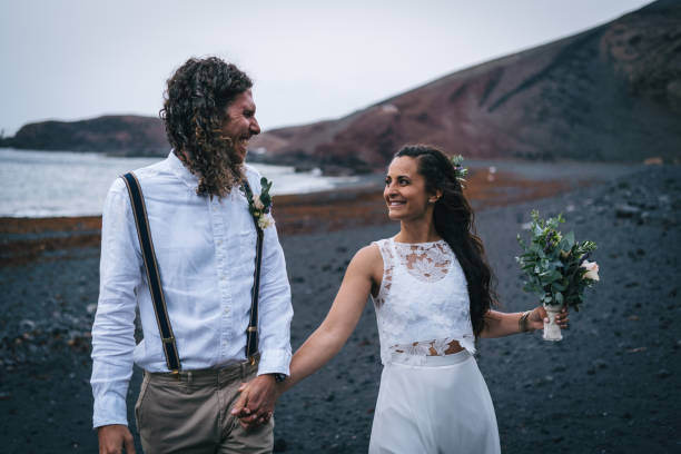 istock Newlyweds hold hands and walk down rocky beach 1326324164