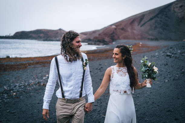 istock Newlyweds hold hands and walk down rocky beach 1326324244