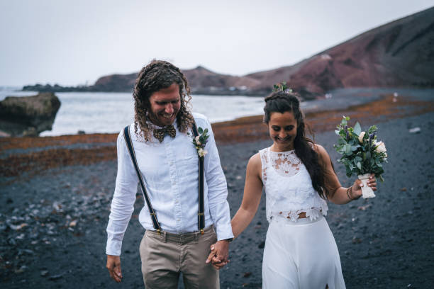istock Newlyweds hold hands and walk down rocky beach 1326324314