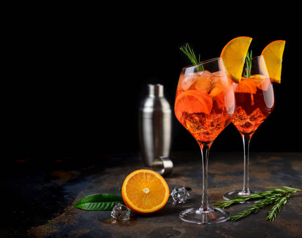 weinglas eiskalten aperol spritz cocktail in einem weinglas serviert, mit scheiben von orange und rosmarin zweig verziert. schwarzer hintergrund - campari stock-fotos und bilder