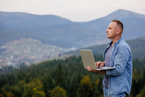 Man working outdoors with laptop in mountains. Concept of remote work or freelancer lifestyle. internet 5G