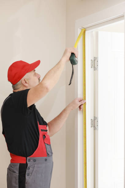 istock Worker in red cap and work suit with the measuring tape. Man is installing the doors. Measure tape in hands. Repair works. Maintenance in the apartment. 1326331578