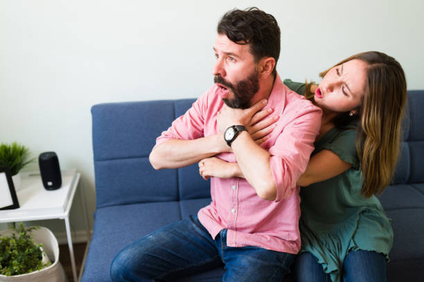 Adult man suffocating with a piece of food Beautiful young woman telling her boyfriend to calm down while doing the Heimlich maneuver in the living room choking stock pictures, royalty-free photos & images