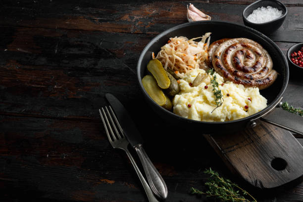 salsichas alemãs tradicionais com purê de batatas e chucrute em frigideira de ferro fundido, em fundo de mesa de madeira escura antiga, com espaço para copyspace de texto - german culture salad prepared potato bratwurst - fotografias e filmes do acervo