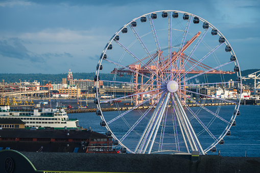 Seattle, USA - Jun 6, 2021: Late in the cloudy overcast Elliott Bay from the Pike Place Market-front with the illuminated Ferris Wheel.