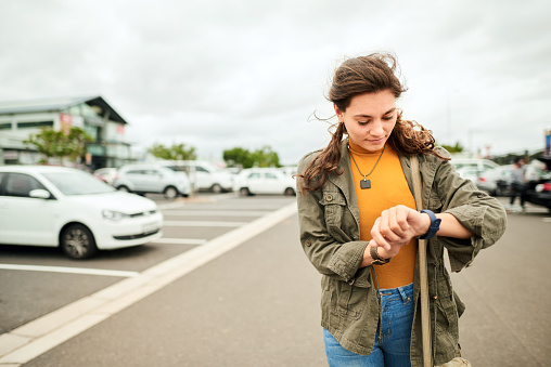 Young woman checking the time on her watch while walking across a parking lot to catch a taxi