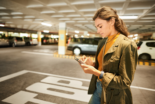 Young woman walking through a parking garage and checking her phone for her taxi pickup location