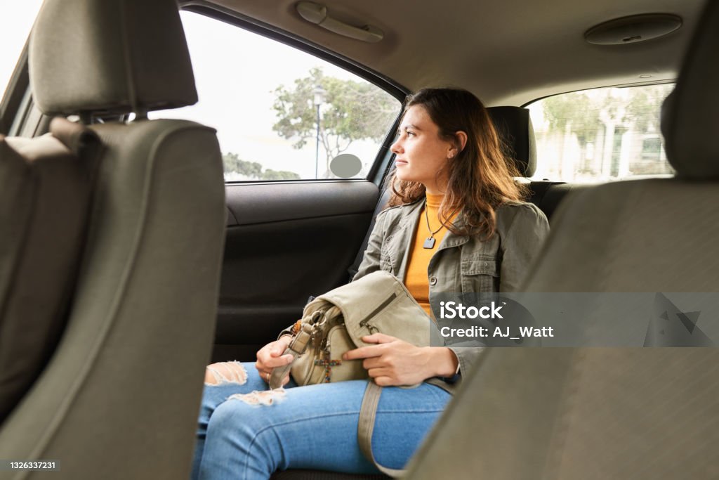 Young woman looking at the passing city from the backseat of a taxi Young woman sitting alone in the back of a taxi and looking out at the passing city Crowdsourced Taxi Stock Photo