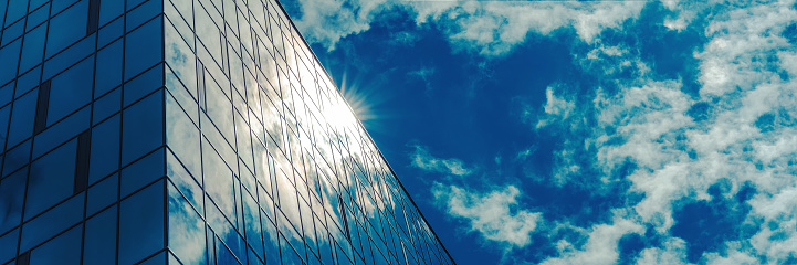 panoramic windows of local commercial building reflect bright sunlight under blue sky with fluffy white clouds