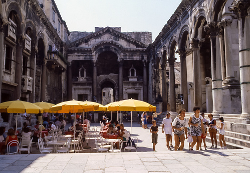 Split, Croatia - aug 1985: tables and umbrellas of a bar set among the millennial colonnades of the Diocletian's Palace in Split.