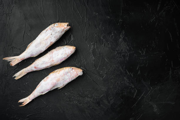 istock Frozen mullet or sultanka fish, on black dark stone table background, top view flat lay , with copy space for text 1326342892