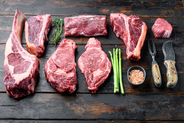 variety of raw beef meat steaks for grilling with seasoning and utensils, tomahawk, t bone, club steak, rib eye and tenderloin cuts, on old dark  wooden table background, with copy space for text - veal t bone steak raw steak imagens e fotografias de stock