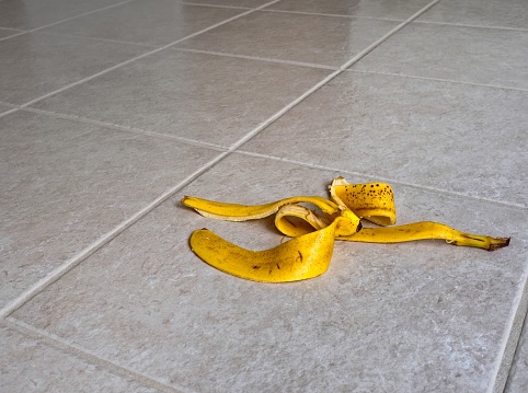 Bright yellow banana on a slippery tile floor. Cliché of slipping on a banana with room for copy space.