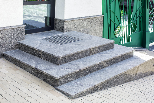granite gray porch step with a foot mat at the entrance to the central door made of glass modern architecture office style close-up with green gate, nobody.