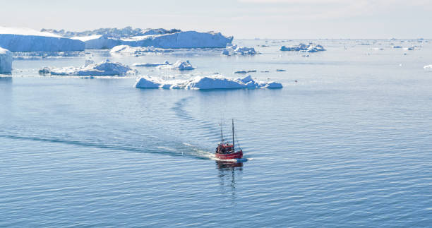 Icebergs and tourist boat in Greenland iceberg landscape of Ilulissat icefjord Icebergs and tourist fishing boat in Greenland iceberg landscape of Ilulissat icefjord with giant icebergs. Icebergs from melting glacier. Aerial drone photo of arctic nature. ilulissat icefjord stock pictures, royalty-free photos & images