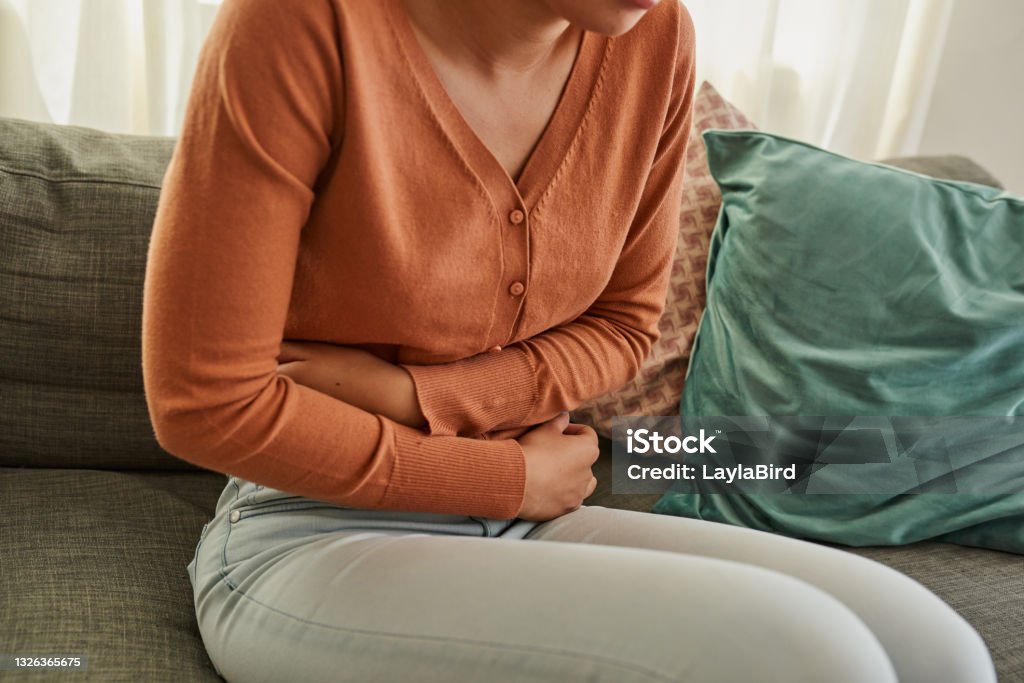 Shot of a woman experiencing stomach pain while lying on the sofa at home I need a heat pad, stat Stomachache Stock Photo
