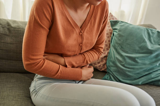 Shot of a woman experiencing stomach pain while lying on the sofa at home stock photo