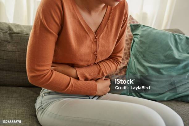 Shot Of A Woman Experiencing Stomach Pain While Lying On The Sofa At Home Stock Photo - Download Image Now
