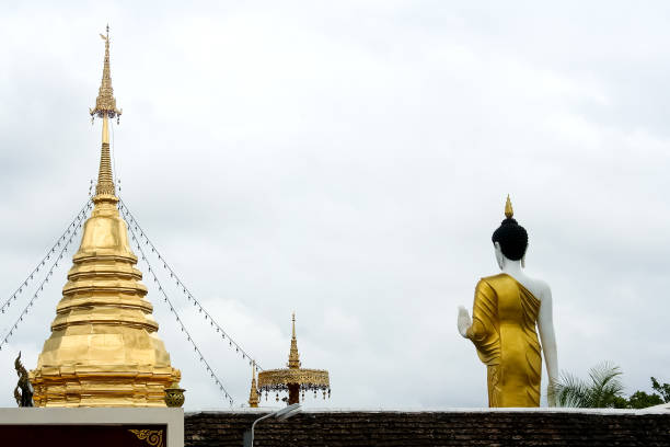 istock Gold pagodaon and Standing Buddha image on white cloud sky background at Wat phra that doi khum  in Chiang Mai of Thailand 1326373043