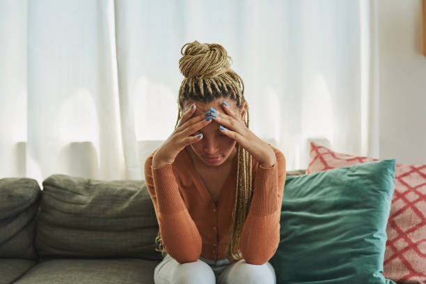 shot of a young woman looking sad on the sofa at home - female emotional stress african ethnicity loss imagens e fotografias de stock