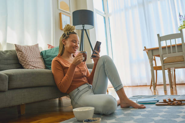 Shot of a young woman using a smartphone and having coffee while working from home