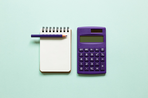 Blank notebook and colored pencil and purple calculator on blue background. top view, copy space