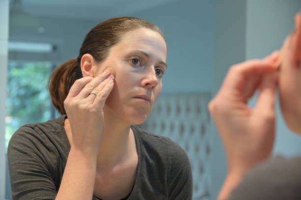 istock Woman applying makeup on her face looking at mirror reflection in bathroom 1326375932