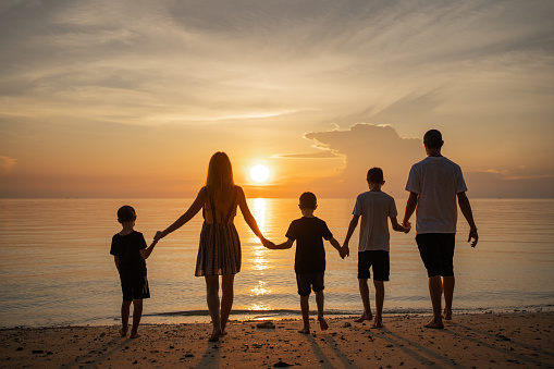 Rear view of family walking with holding hands towards the sea at sunset.