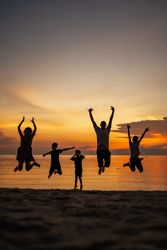 Silhouette of a family joyfully jumping on the beach at sunset.
