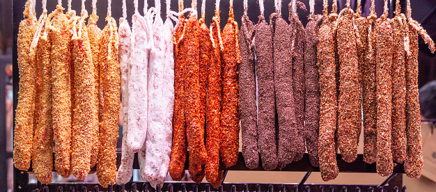 Dried sausages sprinkled with different colors of spices are hung in a row on a market hanger