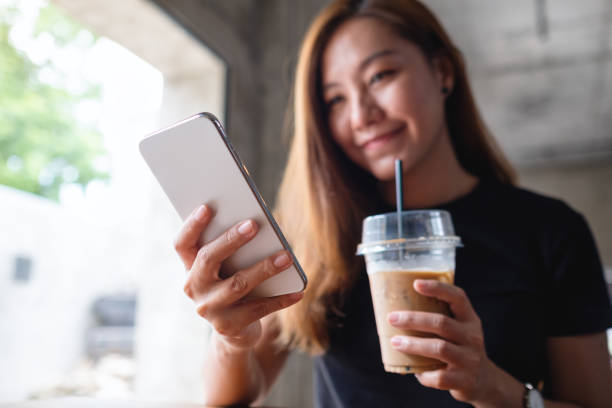 istock a beautiful young asian woman holding and using mobile phone while drinking coffee in cafe 1326394125