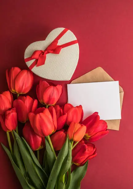Bouquet of red  tulips and gift heart box isolated on red background . Spring flowers. Greeting card for Birthday, Woman, Mother's Day, Wedding, Valentines day. Flat lay. Copy space. Banner