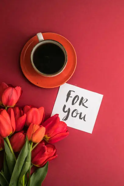 Photo of morning coffee and a bouquet of red tulips on a bright red background. View from above.Copy space for text. The concept of holidays.